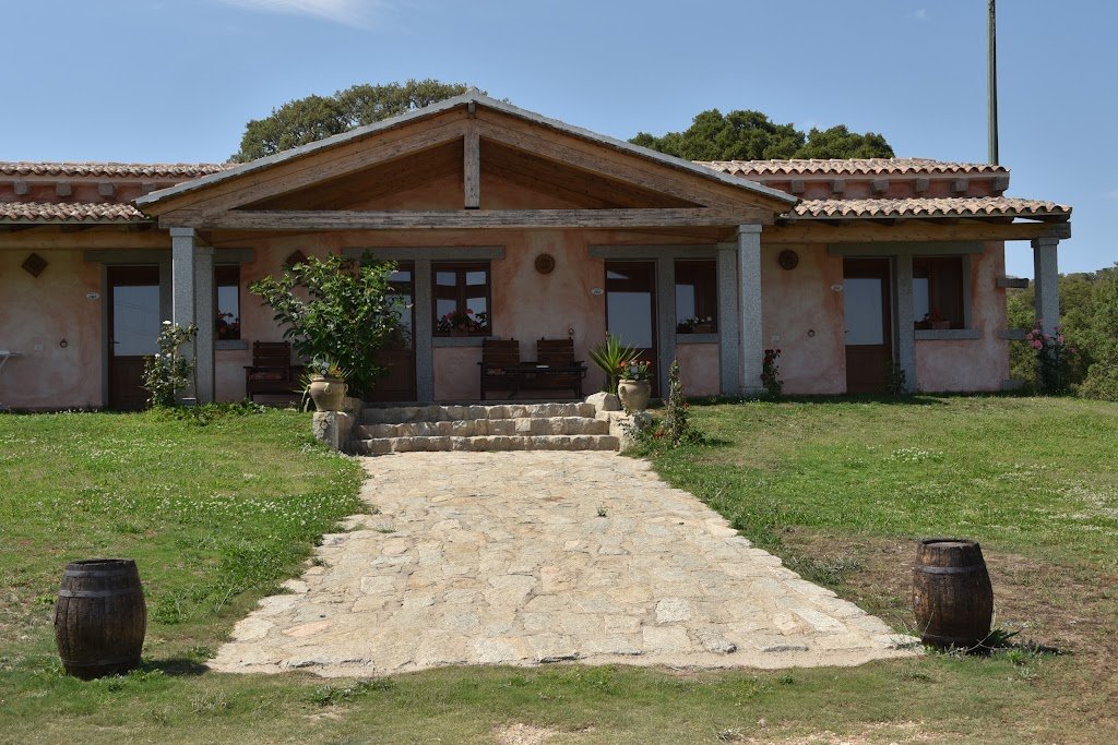 Facciata del casolare dell'agriturismo a Monti con portico in granito, botti e prato