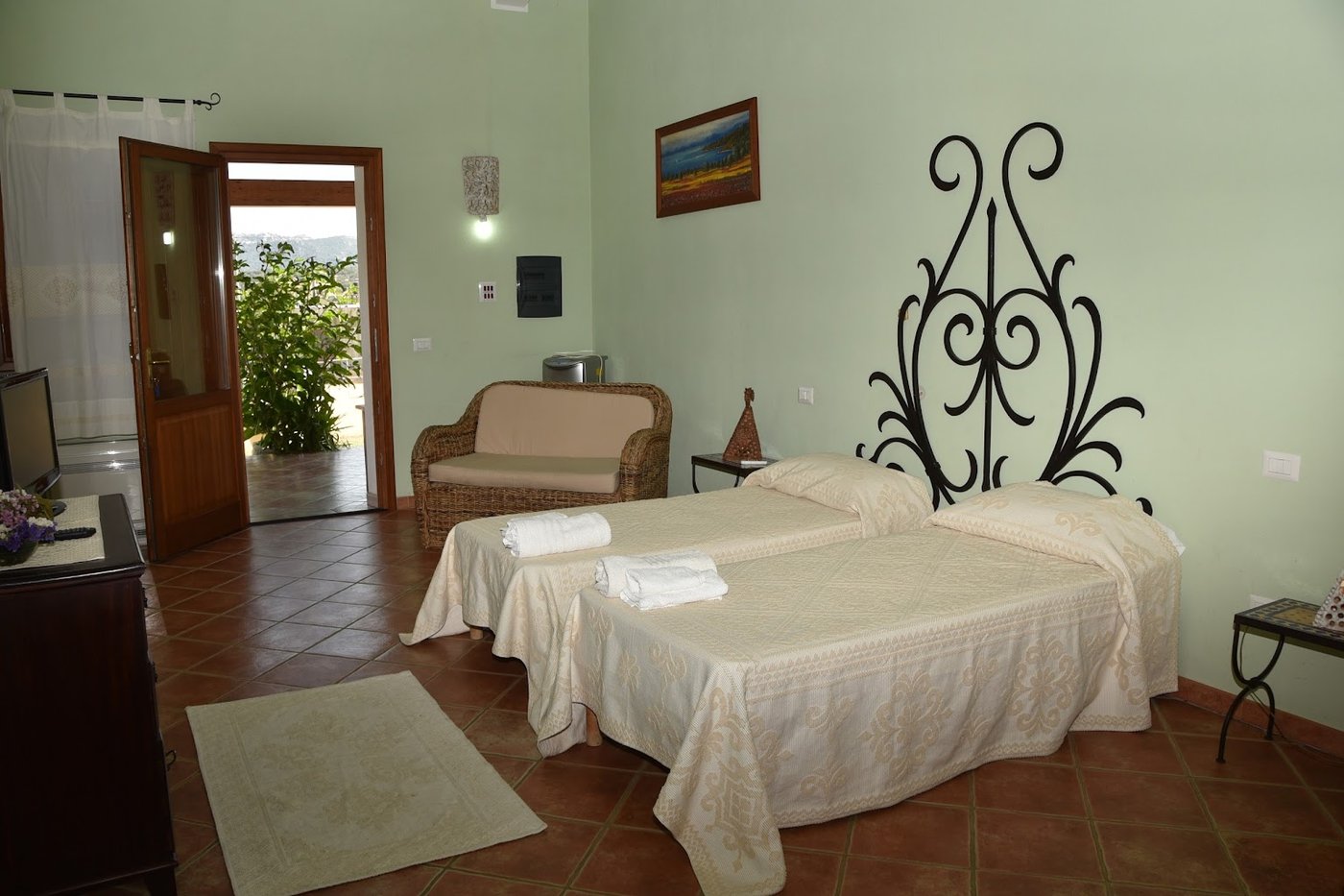 Camera dell'agriturismo a Monti con letti, poltrona in vimini e accesso alla veranda